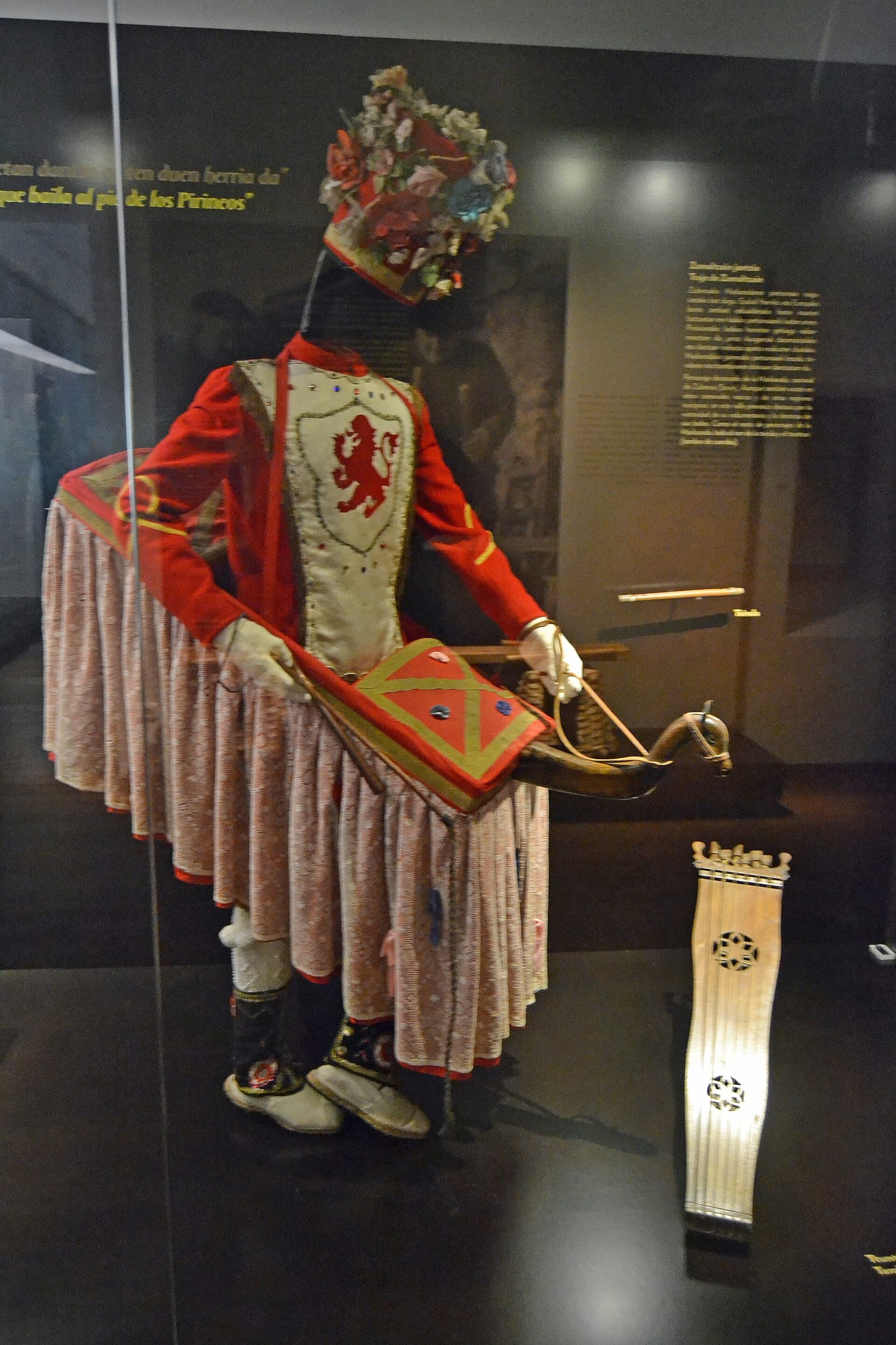 Costume du Zamalzain exposé : veste rouge, haute coiffe fleurie, jupon de dentelle autour du cheval de bois.